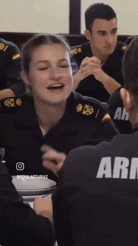 a woman in a military uniform is laughing while sitting at a table with other people .