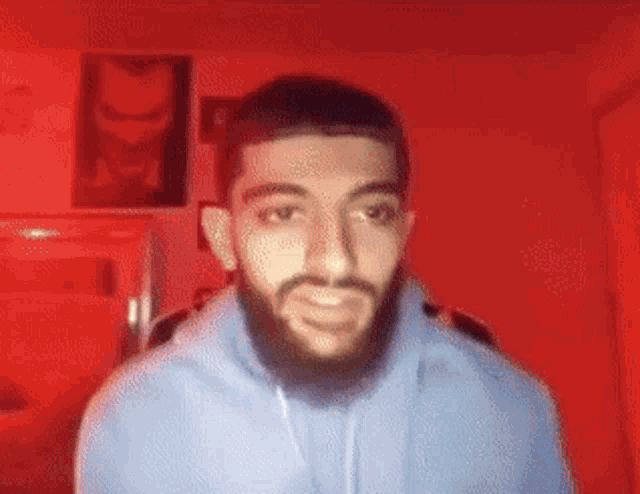 a man with a beard is standing in front of a red wall and smiling .