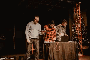 three men standing in front of a table with a laptop on it and a christmas tree in the background