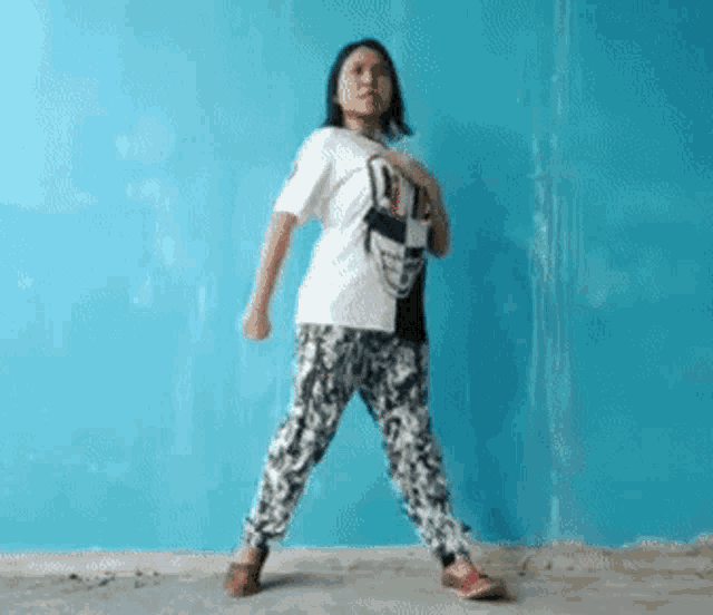 a woman wearing a white shirt with a skull on it is dancing in front of a blue wall