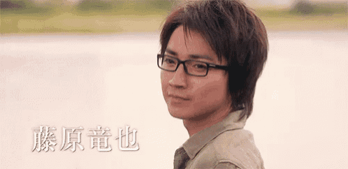 a young man wearing glasses is looking at the camera with chinese writing behind him .