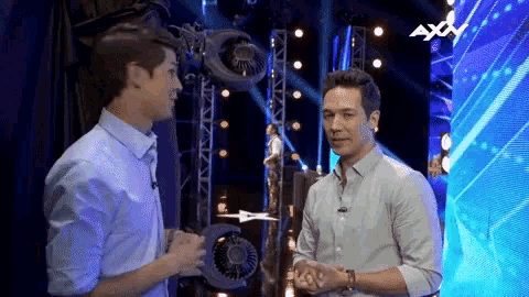 two men are talking in front of a screen that says axv on it