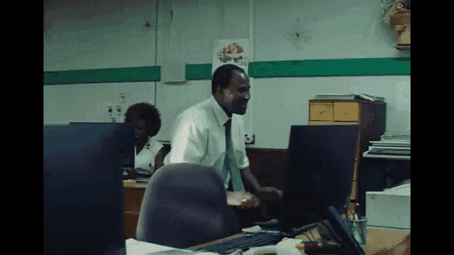 a man in a white shirt and tie is standing in front of a computer screen .