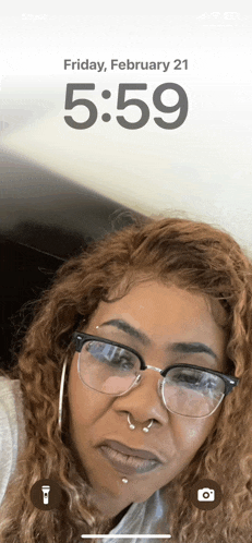 a woman wearing glasses and a nose ring shows the time as 5:59