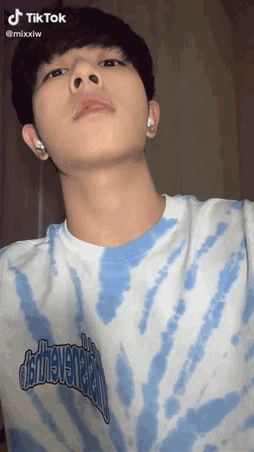 a young man wearing a blue and white tie dye t-shirt looks up at the camera with a tiktok watermark