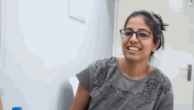 a woman wearing glasses and a gray versace shirt smiles