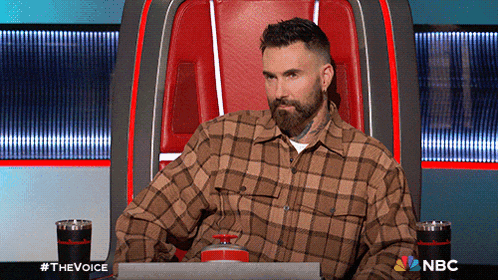 a man in a plaid shirt is sitting in a chair with a nbc logo behind him