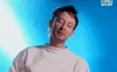 a man in a white sweater is standing in front of a blue wall .