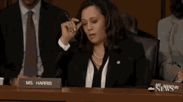 a woman in a suit and tie is sitting at a table with a name tag that says ms. harris .