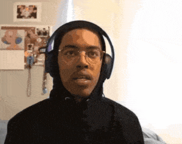 a young man wearing headphones and a black hoodie looks at the camera