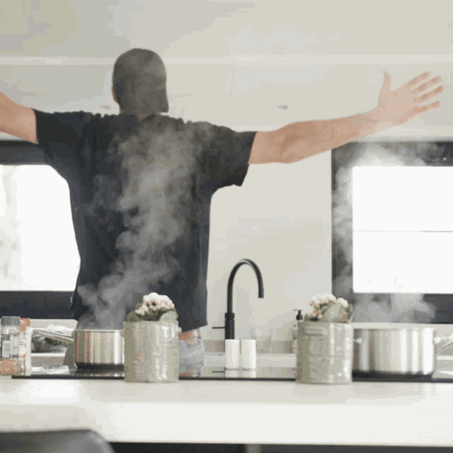 a man stands in a kitchen with his arms outstretched and steam coming out of the pots