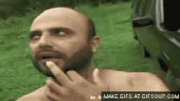 a bald man with a beard is making a funny face while holding his finger to his mouth .