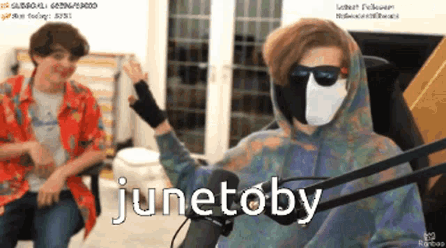 a man wearing a mask and sunglasses is sitting in front of a microphone with the words junetoby written on it