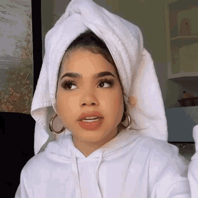 a woman with a towel wrapped around her head is wearing a white hoodie and hoop earrings .