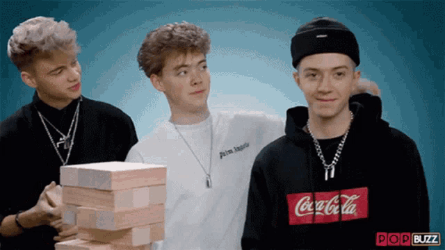 a man wearing a coca cola sweatshirt is playing jenga with two other men