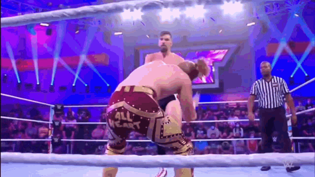 two men are wrestling in a wrestling ring while a referee looks on .