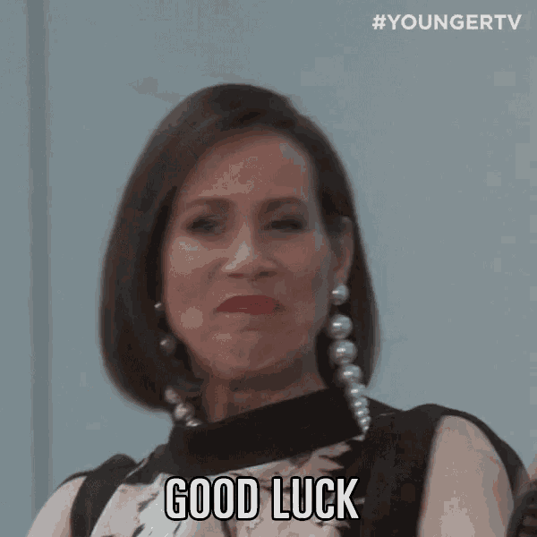 a woman wearing pearls and a black top says good luck