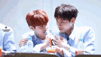 a couple of boys sitting next to each other with a bottle of water between them