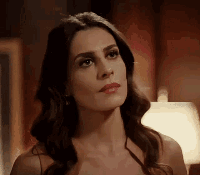 a woman with long dark hair and red lipstick is looking at the camera in a dark room .