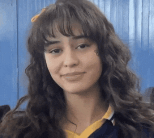 a girl with long brown hair and bangs is wearing a yellow shirt and a blue shirt