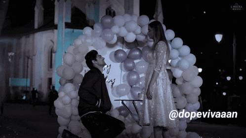 a man kneeling down in front of a woman with balloons around them