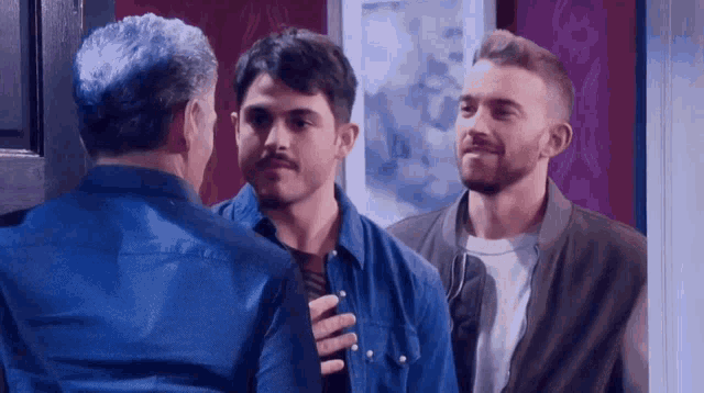 three men are standing next to each other and one of them is wearing a blue shirt