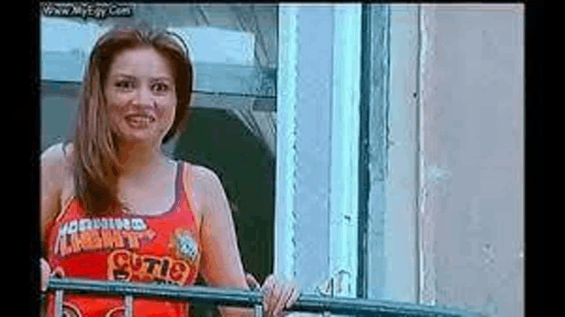 a woman in a red tank top is standing on a balcony looking out a window .