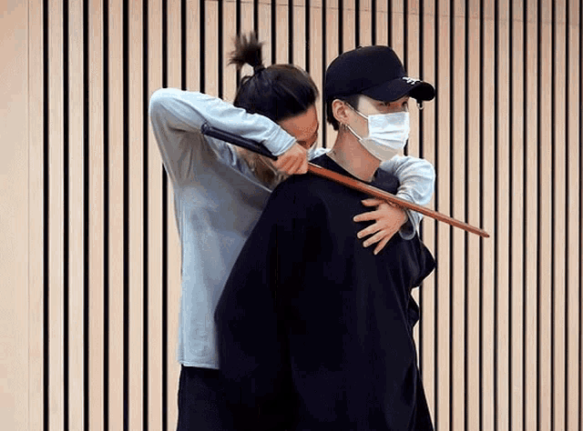 a man wearing a mask is holding a stick over another man 's shoulder