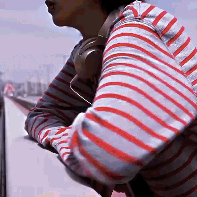 a person wearing headphones and a striped shirt looks out over a railing