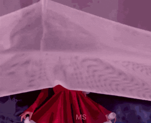 a woman in a red dress is holding a microphone while standing under a white cloth .