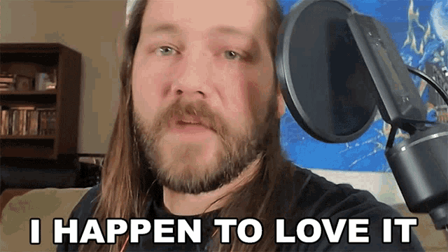 a man with a beard stands in front of a microphone and says i happen to love it