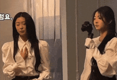 a woman in a white shirt is holding a camera while another woman looks on .