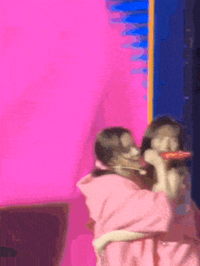 a woman in a pink hoodie is eating a slice of pizza