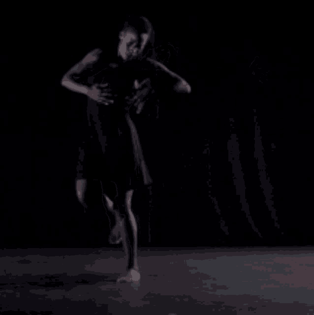 a woman in a black dress is dancing in front of a black curtain .