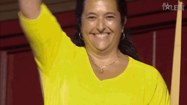 a woman in a yellow shirt is smiling and raising her arm in front of a sign that says talent