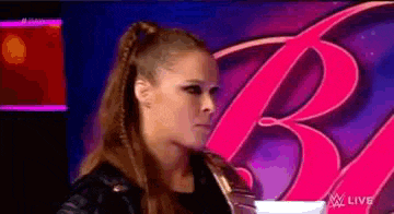 a woman in a black jacket is standing in front of a pink letter b .