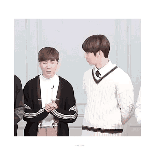 two young men are standing next to each other in front of a white wall .