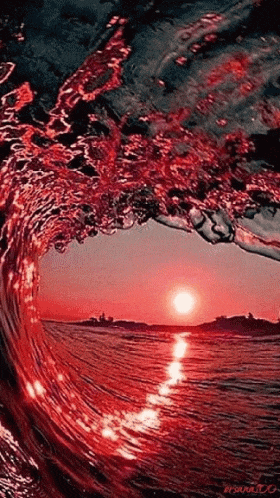 a red wave in the ocean at sunset with the sun shining through it