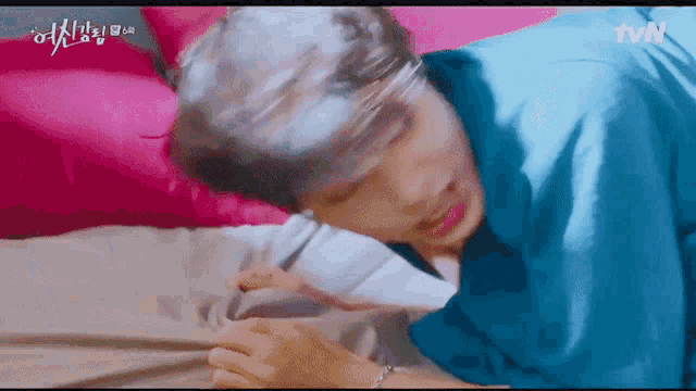 a man is laying on a bed with a pink pillow and a blue shirt on .