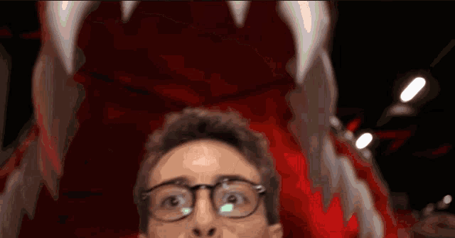 a man wearing glasses is looking up at a red monster