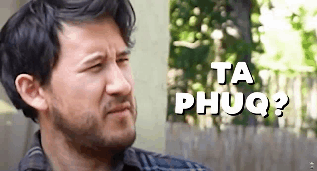 a man with a beard is standing in front of a sign that says ta phuq ?