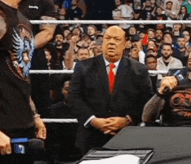 a man in a suit and tie is sitting at a table in front of a crowd .