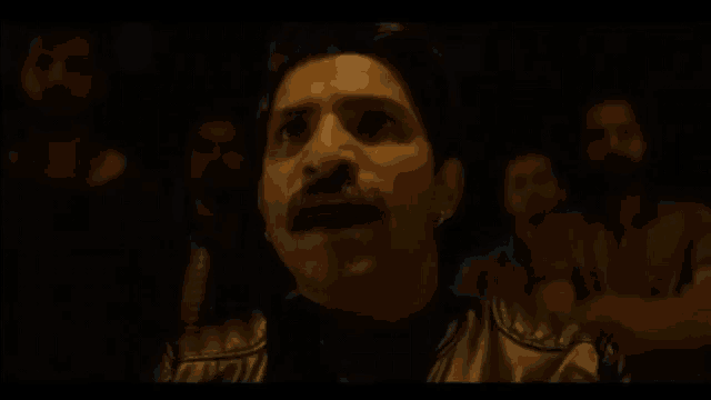 a man with a mustache is sitting in front of a group of people .