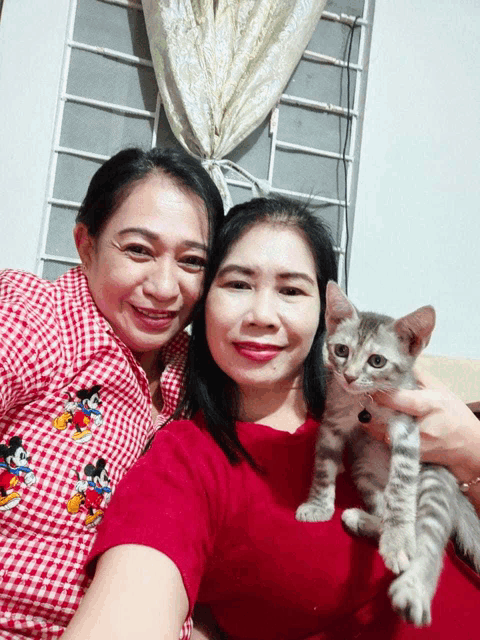 two women posing for a picture with a cat