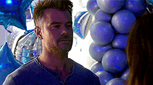 a man is standing in front of a bunch of blue balloons and looking at a woman .