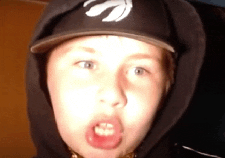 a young boy wearing a hat and a hoodie making a funny face .