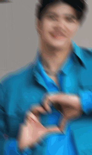 a blurry picture of a man wearing a blue shirt making a heart shape with his hands .