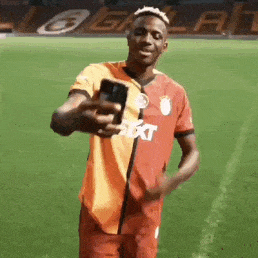 a soccer player is taking a selfie with his phone on a soccer field .
