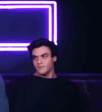 a young man is standing in front of a purple neon sign .
