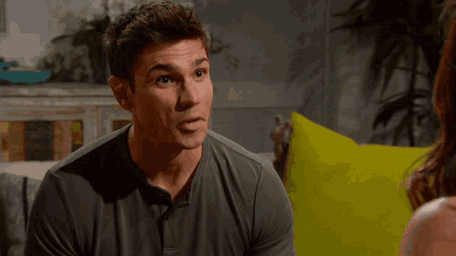 a man in a grey shirt is looking at a woman in a yellow pillow